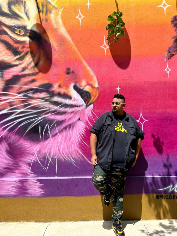 DJ Adrennaa standing in front of a colorful mural of a tiger